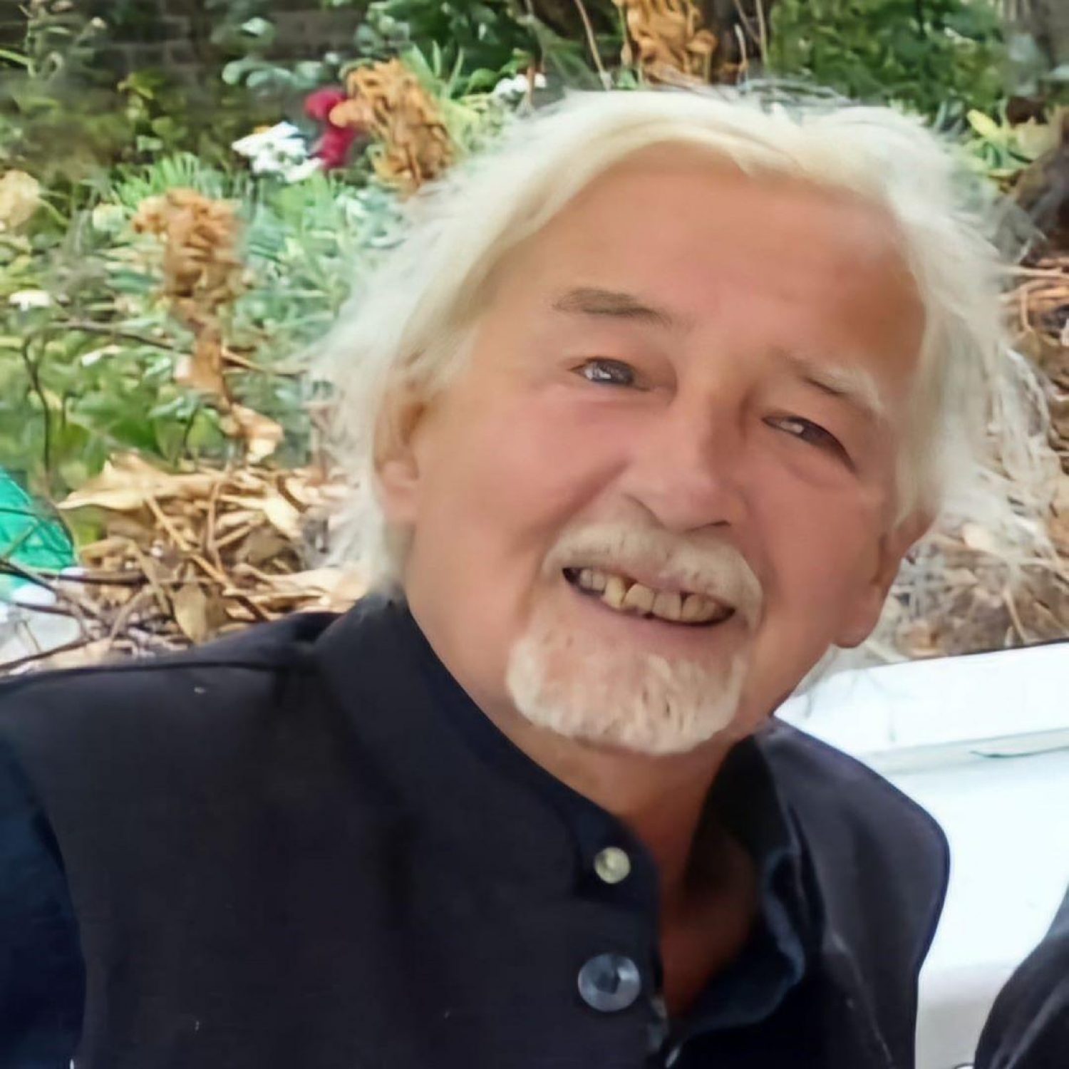 Denis, Poppy's client, man with white hair and beard, blue shirt, garden behind him.