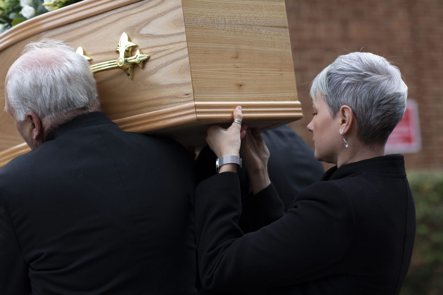 Funeral director and bearers in black carrying wooden coffin
