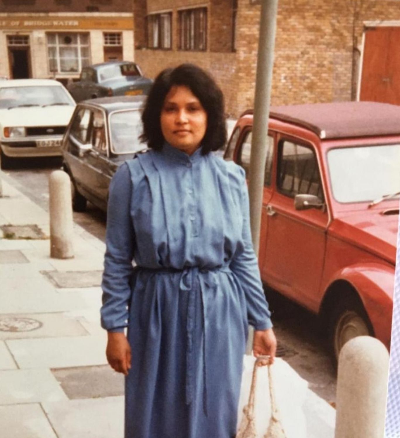 Woman in blue dress with red car behind her
