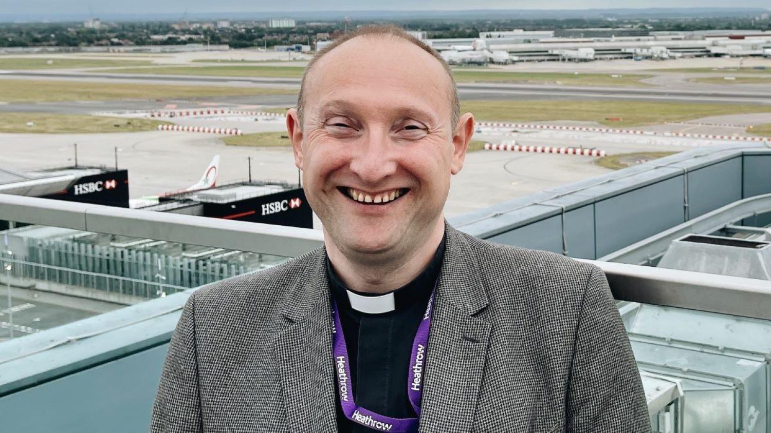 Airport chaplain Bruce Rickards outside with view of Heathrow buildings and runaways behind him