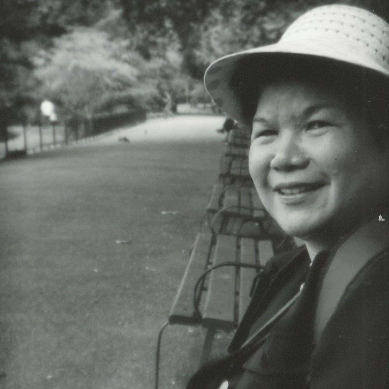 Black and white photo of older Chinese woman in summer hat sitting on a bench