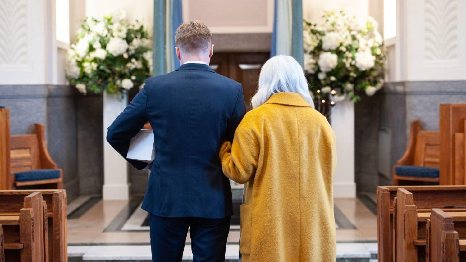 A younger man and older man with backs to the camera approaching the front of a crematorium