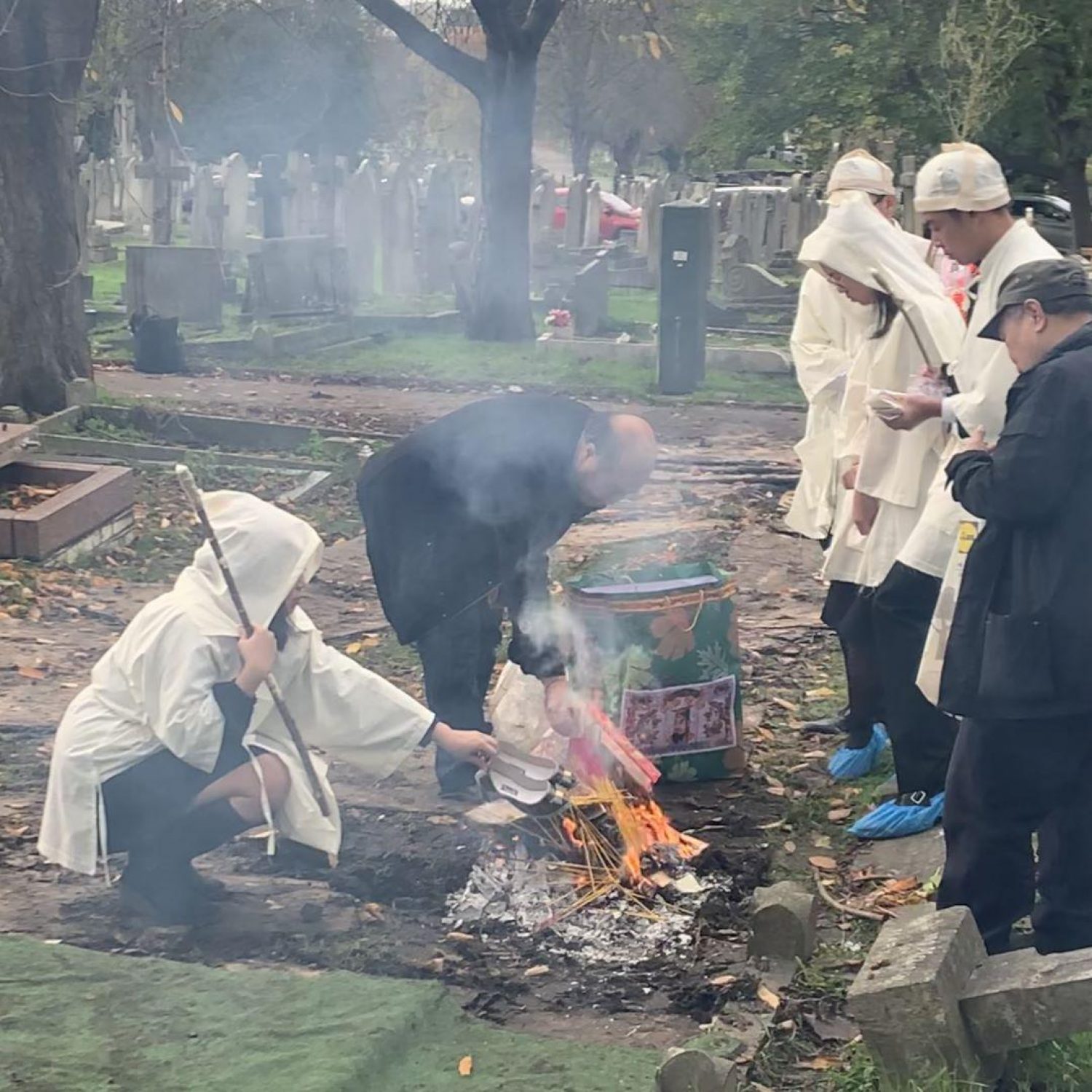 Taoist funeral ceremony with people dressed in white burning incense at the graveside