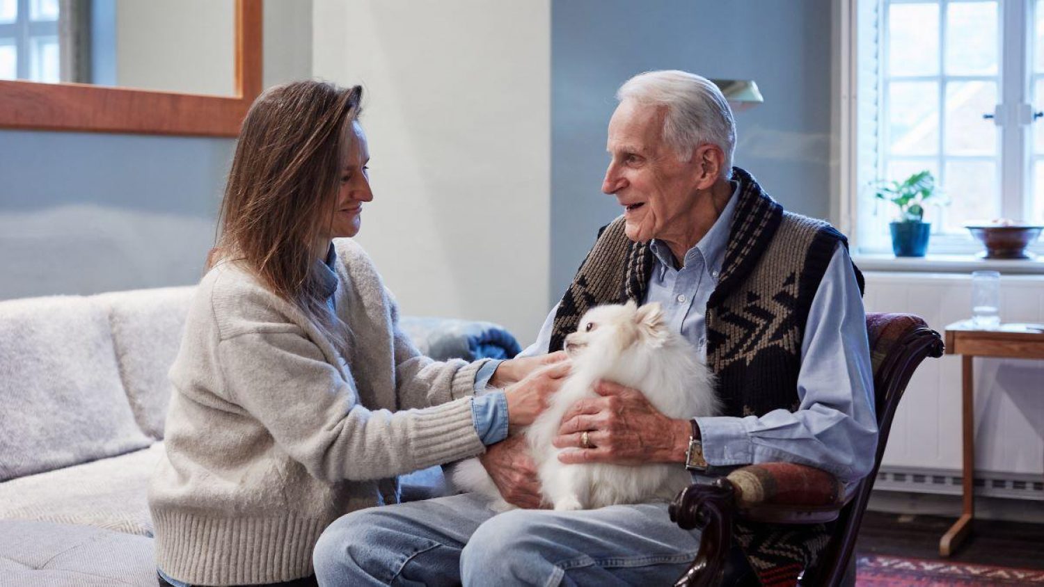 Katie Fyfe, white woman with brown hair and white jumper, with her father, older white haired man, smiling, he is holding a small fluffy white dog