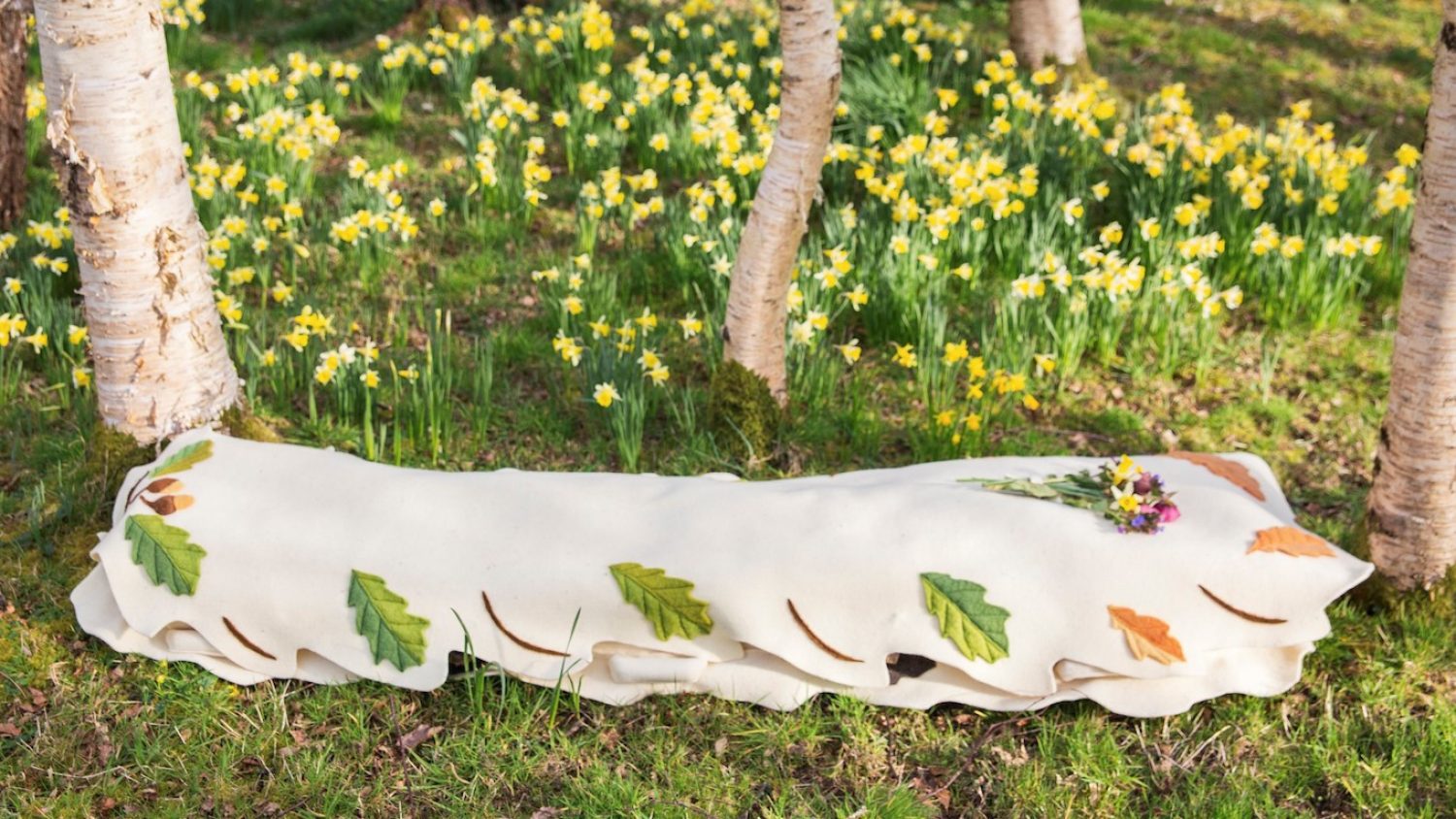 Leaf cocoon woollen coffin made by Bellacouche, on grass with trees and daffodils around