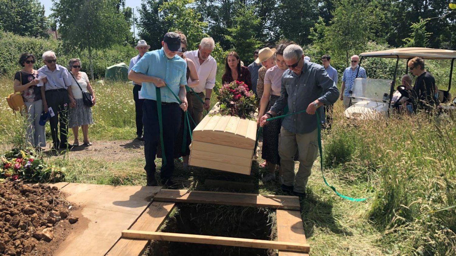 A group of people lowering a pine coffin into a grave at a natural burial site