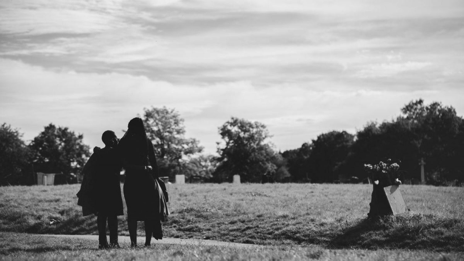 Black and white image, two women with backs to camera beside a grave