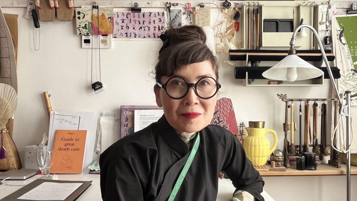 Humanist celebrant Tamiko O'Brien dressed in black with black framed glasses in her studio
