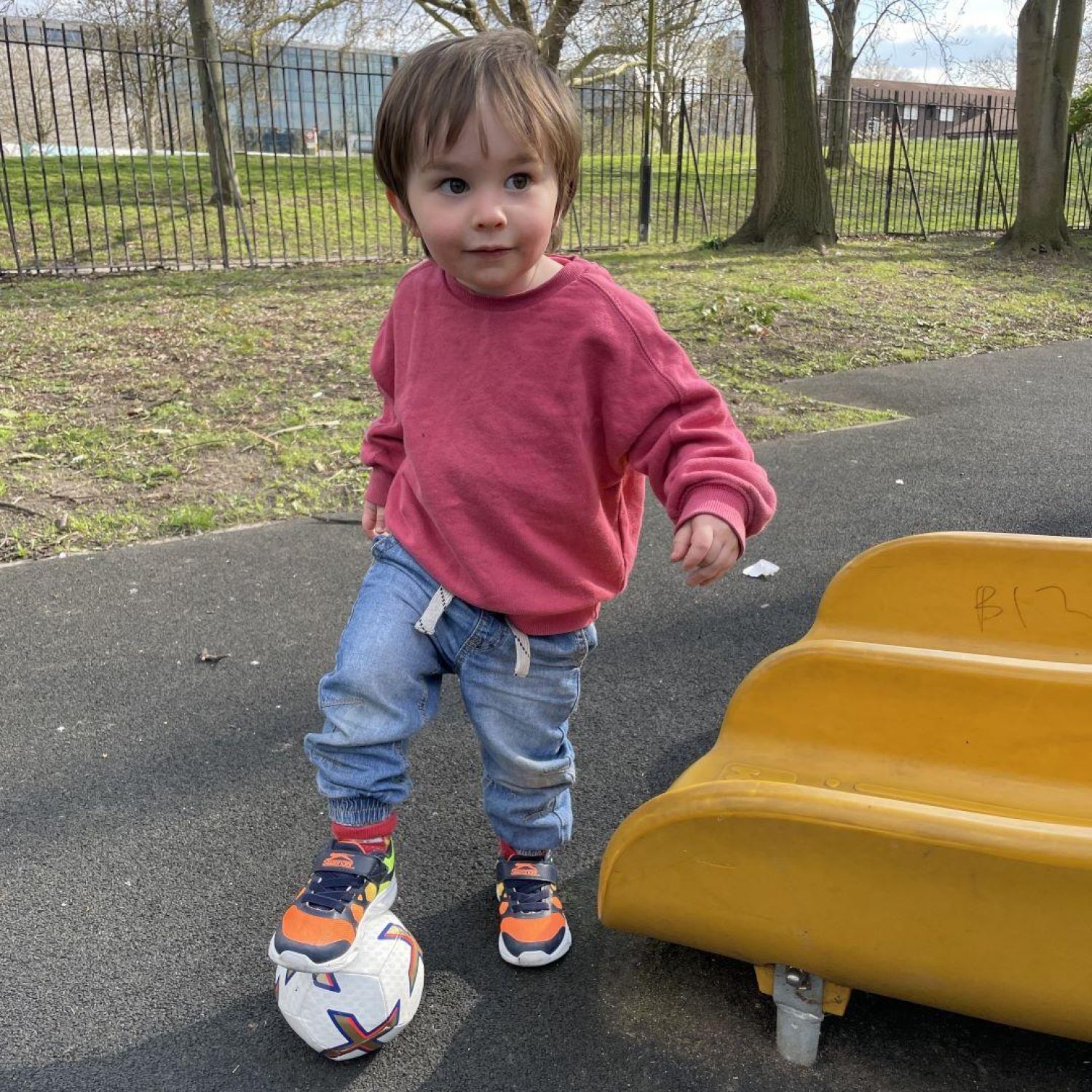 Two year Teddy by a yellow slide in red jumper and jeans