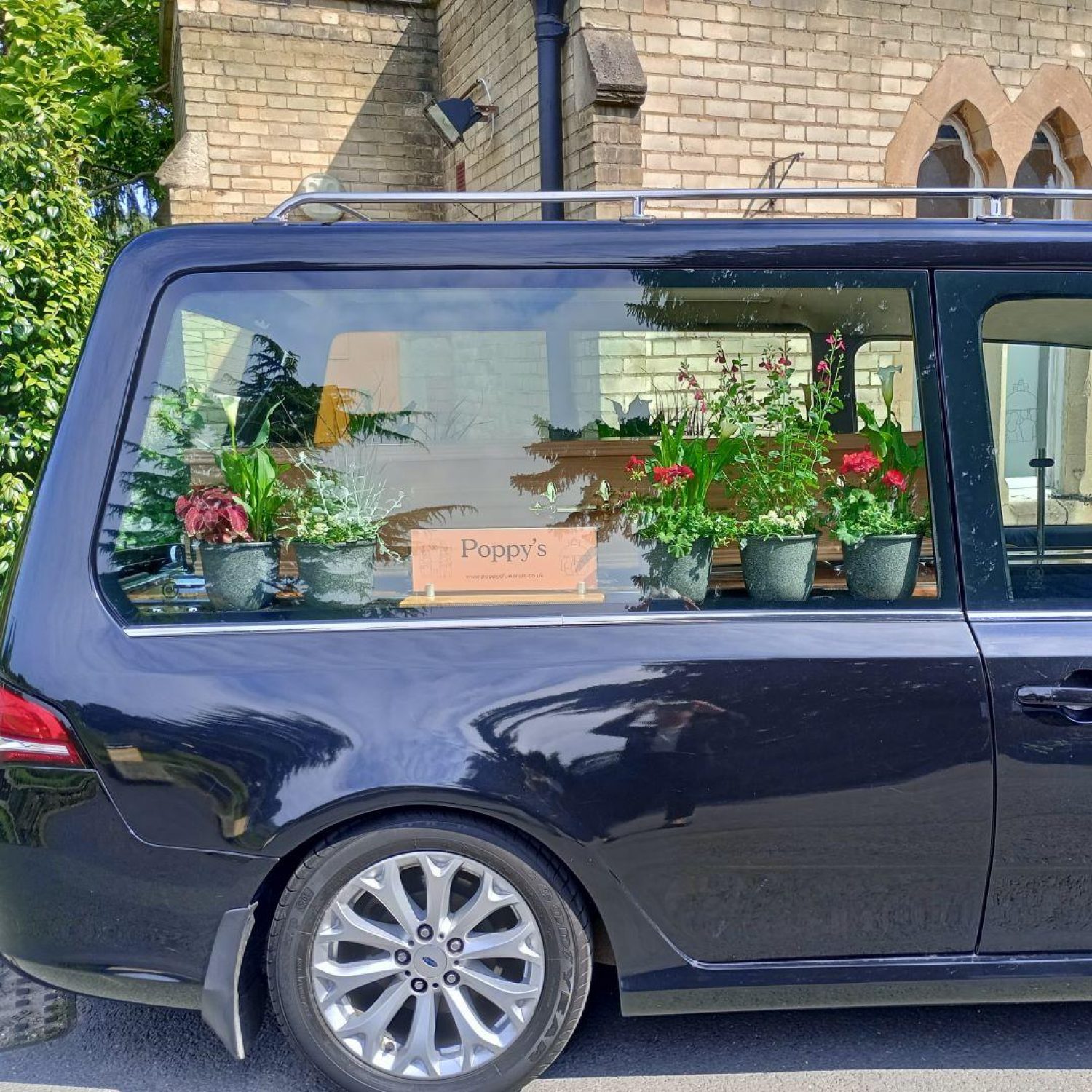 Black hearse with red flowers and Poppy's sign