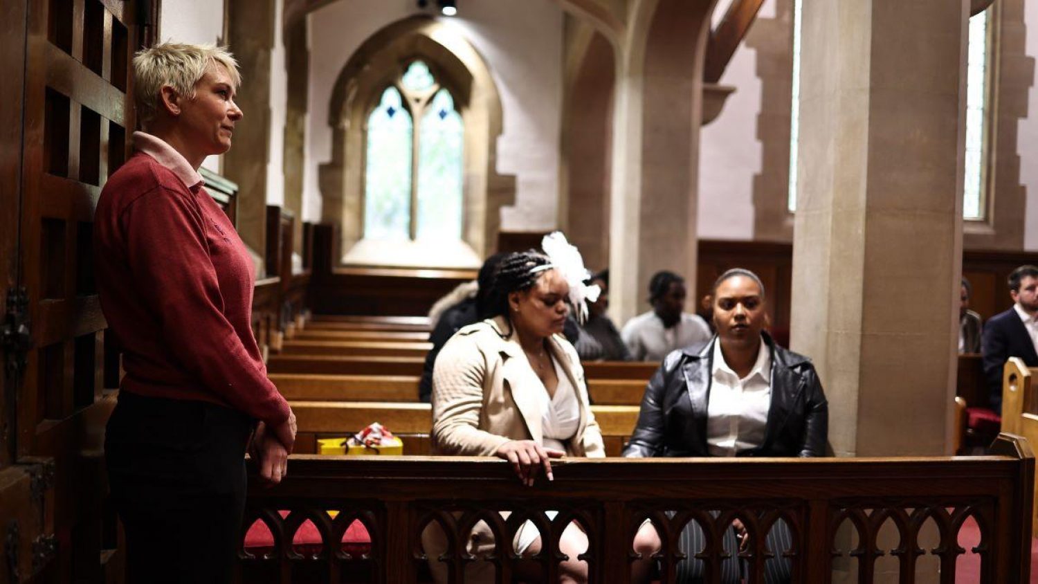 Church funeral: two women in pew, Poppy's team member standing