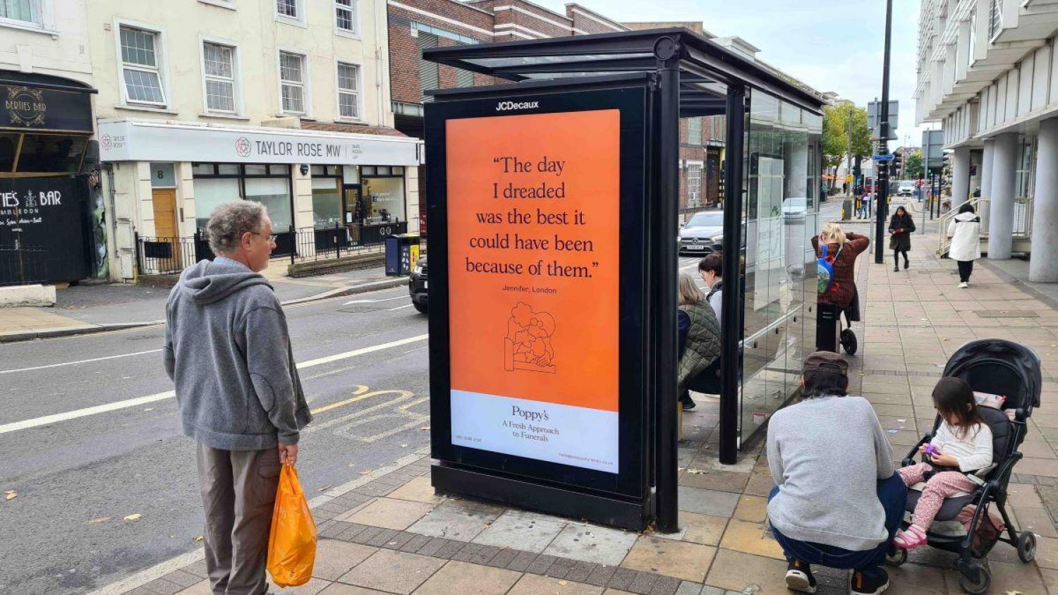 Man at bus stop in London looking at Poppy's advert which says 'The day I dreaded was the best it could have been because of them.'