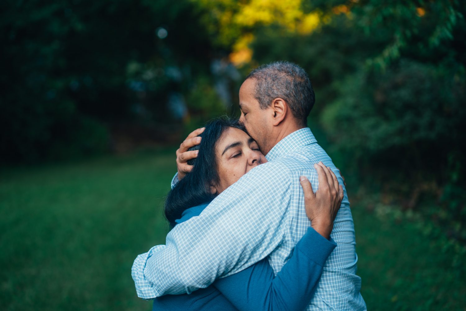 man and woman hugging, surrounded by trees and grass