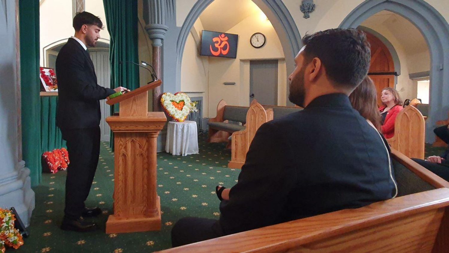 Young man at lectern at funeral service, people in pews listening