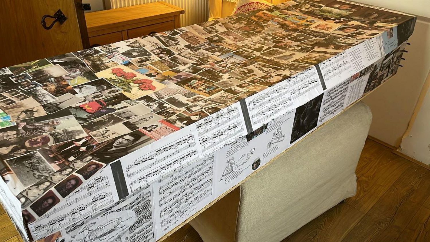 Cardboard coffin with photos and sheet music glued on to it.