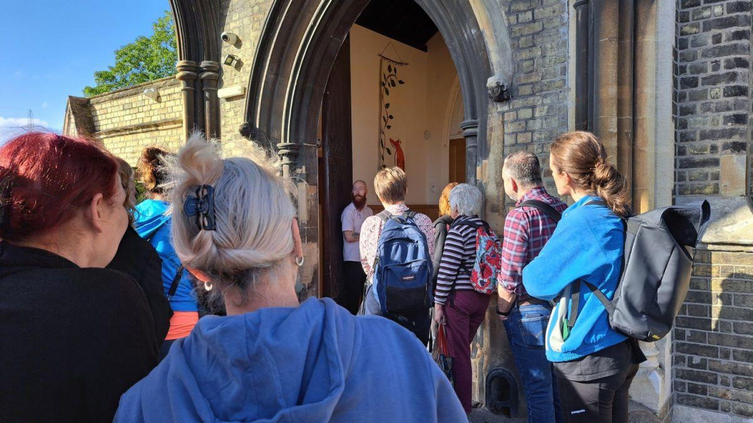 Crowd of people in sunshine walking in through open door of Poppy's mortuary in old chapel in Lambeth Cemetery