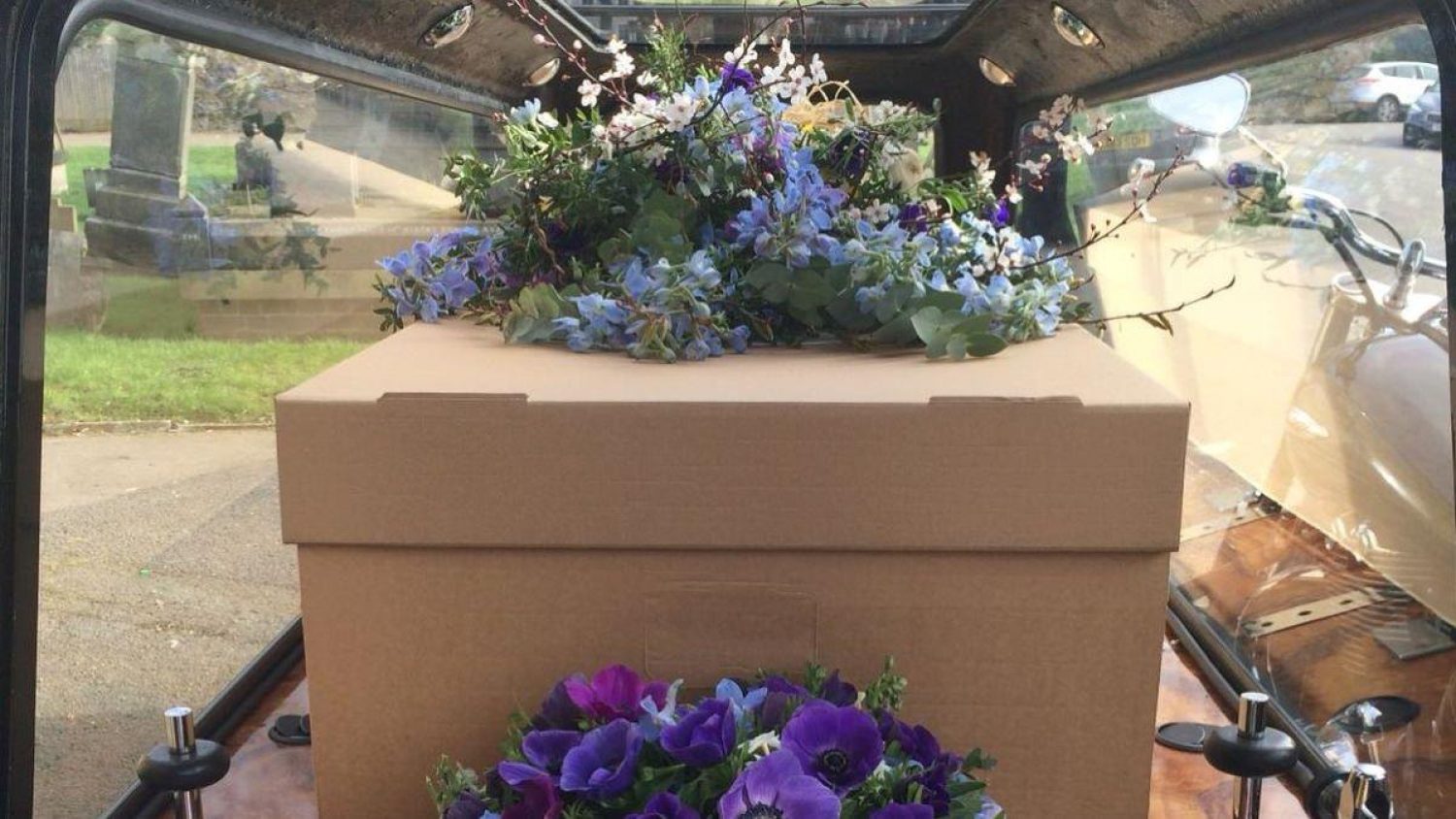 Cardboard coffin with flowers on in hearse.
