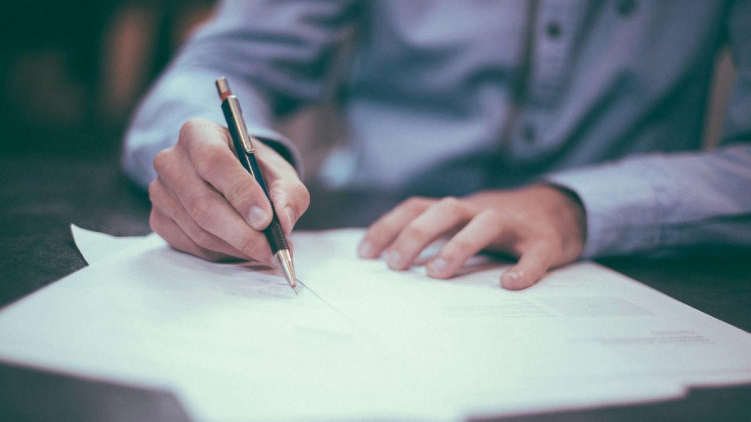 A man's hands with a pen signing paperwork