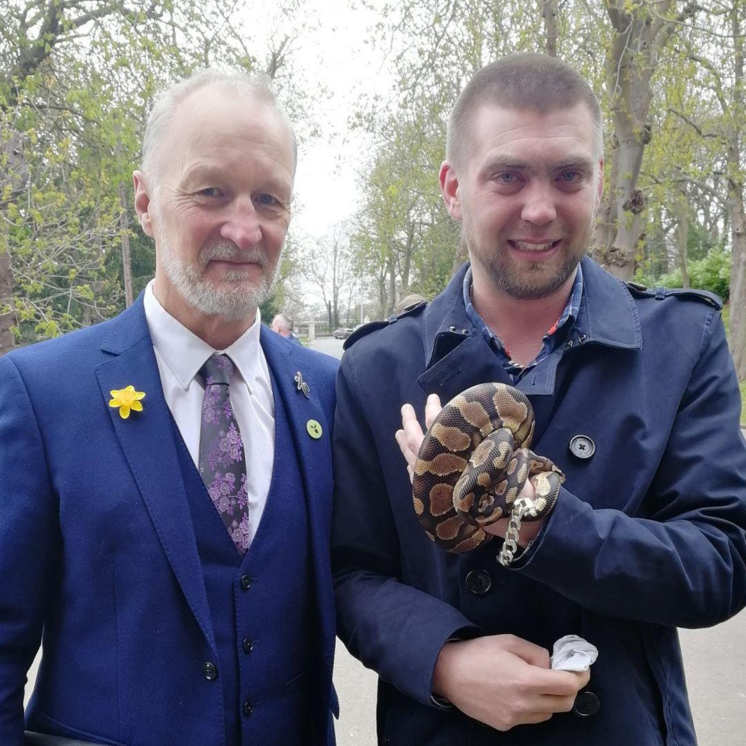 Two men in suits, one holding a black and brown patterned snake