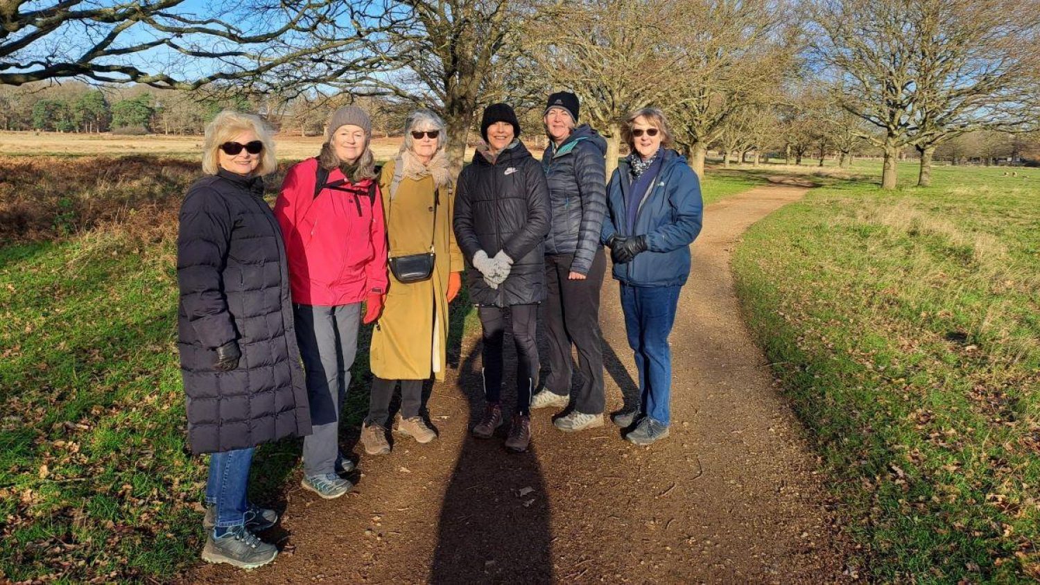 Group of people on sunny winter day in Richmond Park, trees and grass behind them