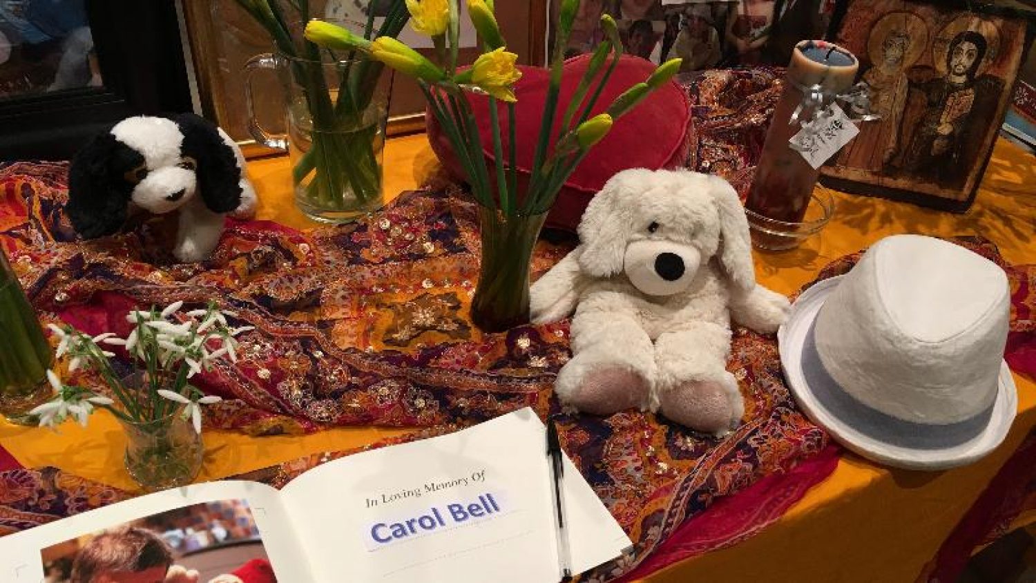 Table with book and pen, white hat, soft toys, daffodils and snowdrops - centrepiece at L'Arche funeral