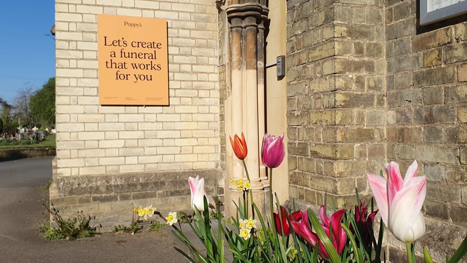Sign saying: Let's create a funeral that works for you, with flowers outside Poppy's Tooting HQ