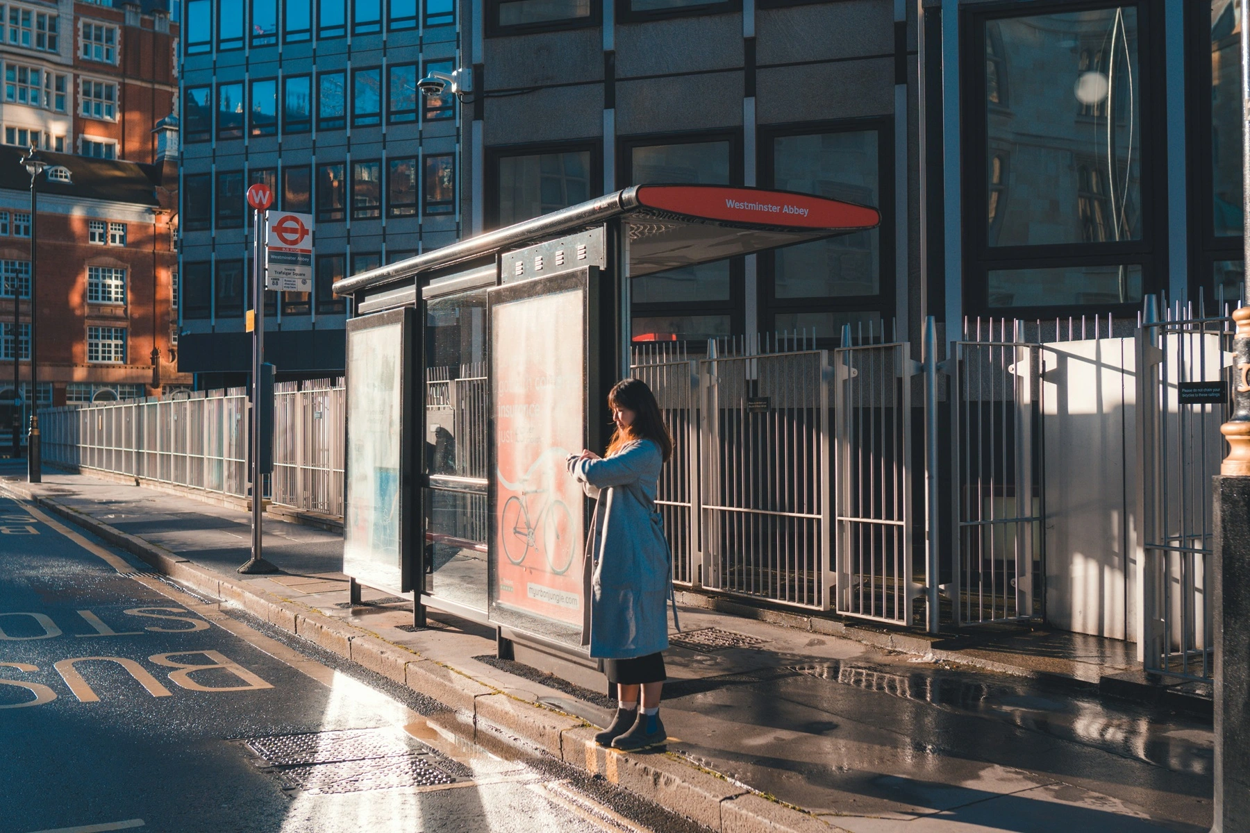 A woman stands at a bus stop alone looking at her watch